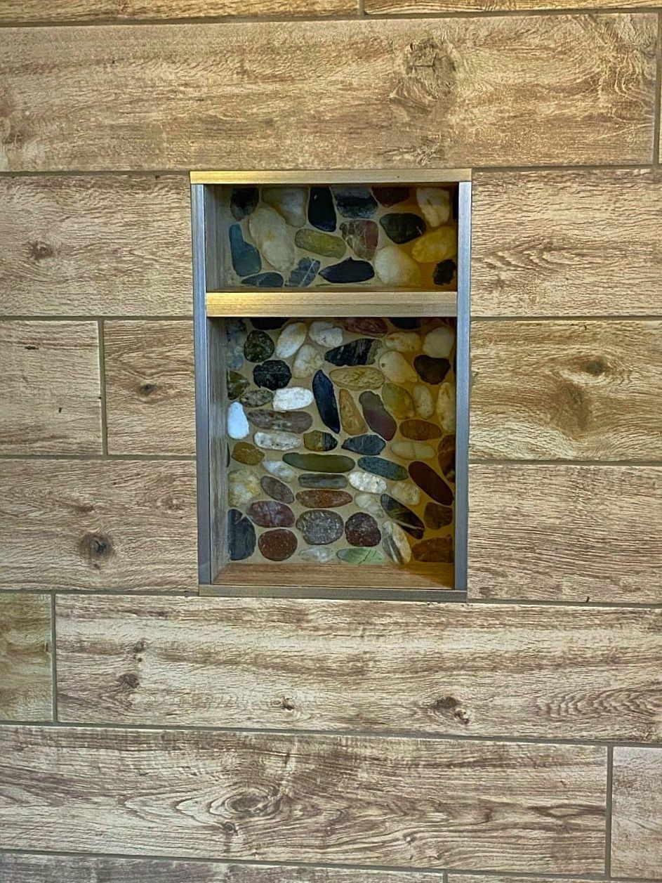 Built-in shower shelf with a riverstone background.