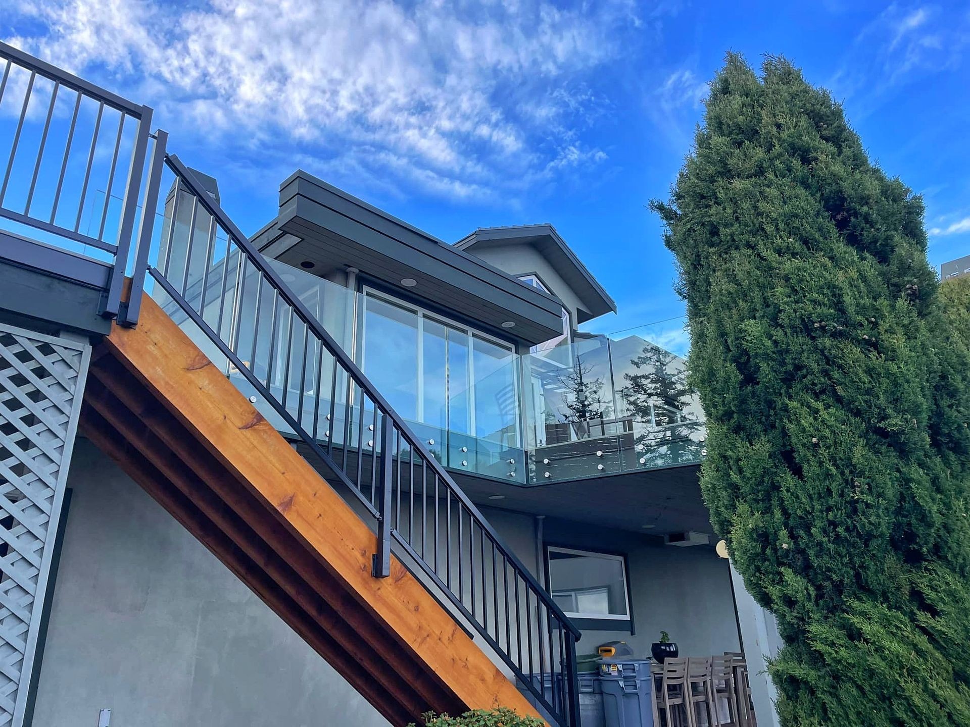 A sturdy wooden staircase with black metal railings connecs an elevated composite deck with the backyard of a home.