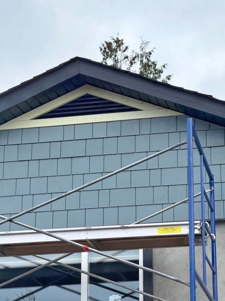 Exterior of a house with blue siding, attic vent, and metal scaffolding in front.